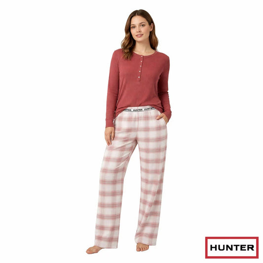 Woman wearing Hunter burgundy pink and green plaid trouser pyjama set with long-sleeve waffle Henley top standing in a cozy room.