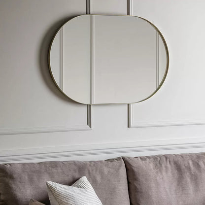 Gallery Hurston Elipse Champagne Mirror with smooth iron frame mounted vertically on a neutral living room wall