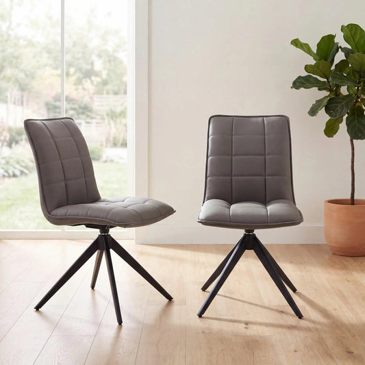 Pair of Indus Valley Skylar grey faux leather dining chairs featuring square grid stitching and black metal 360-degree swivel spider legs.