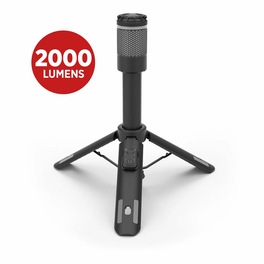 Black Infinity X1 2000 lumen rechargeable camp light mounted on an extended 1.9 meter telescoping tripod illuminating a dark grassy campsite at night.