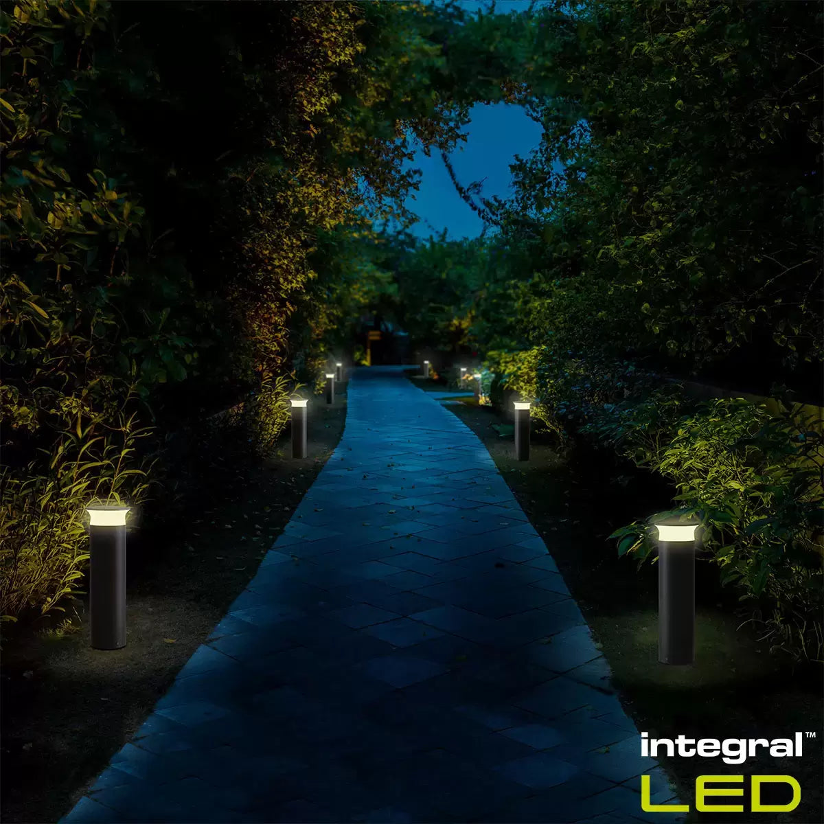 Modern black Integral outdoor bollard light standing on a paved garden path at night.