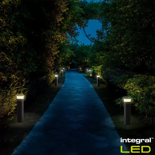 Modern black Integral outdoor bollard light standing on a paved garden path at night.