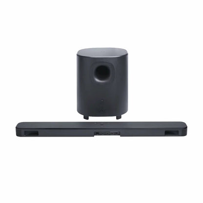 JBL BAR 500MK2 black 5.1 channel soundbar mounted under a wall-mounted TV with its 10-inch wireless subwoofer positioned on a hard-wood floor.