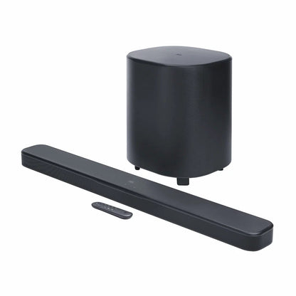 JBL BAR 500MK2 black 5.1 channel soundbar mounted under a wall-mounted TV with its 10-inch wireless subwoofer positioned on a hard-wood floor.
