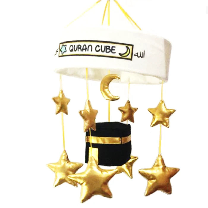 White baby cot mobile attached to a wooden crib rail featuring a plush central Kaaba surrounded by hanging golden stars and crescent moon plushies.