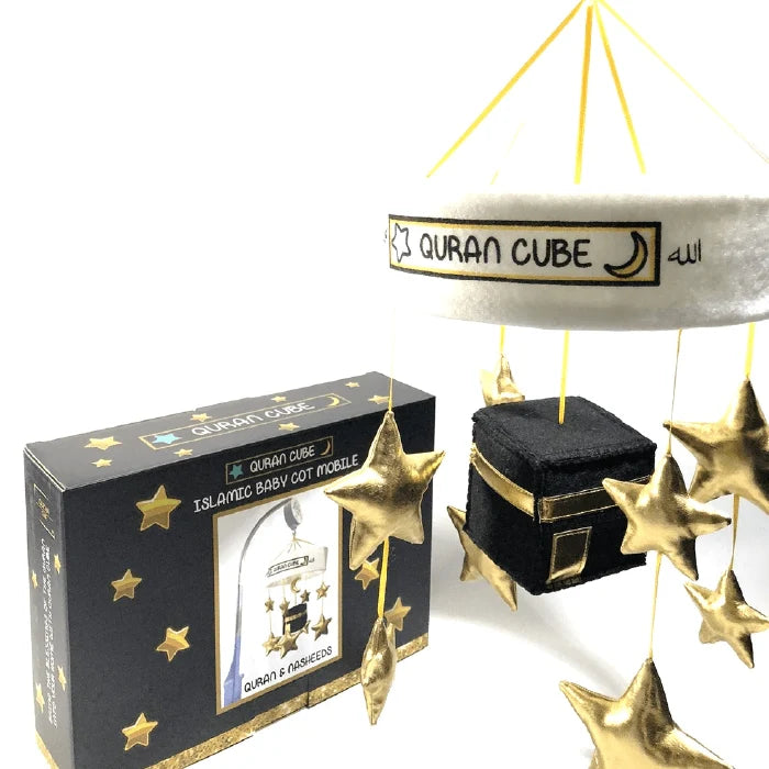White baby cot mobile attached to a wooden crib rail featuring a plush central Kaaba surrounded by hanging golden stars and crescent moon plushies.