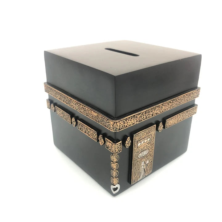 Front angle view of the 9cm black and gold hand-painted Kaaba Sadaqa money box resting on a wooden tabletop.