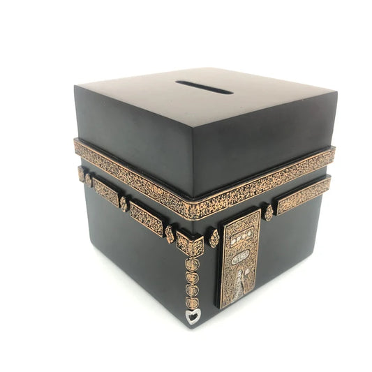 Front angle view of the 9cm black and gold hand-painted Kaaba Sadaqa money box resting on a wooden tabletop.