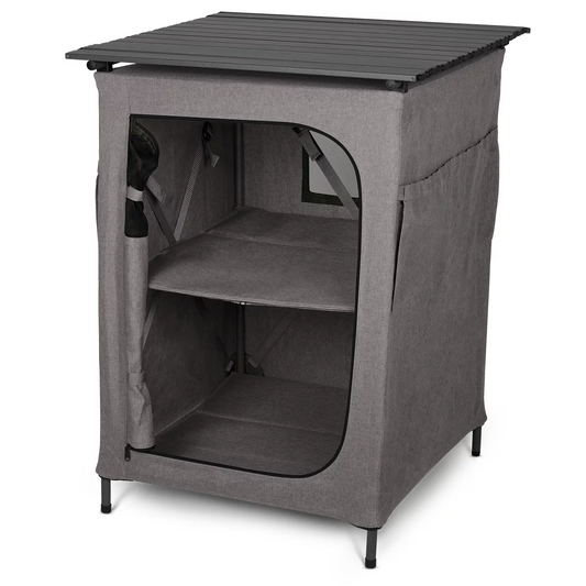 A sleek grey Kampa Hollow folding camping cupboard standing inside a large tent, showing its two fabric shelves packed with neatly folded clothes and a lantern resting on its solid top side table surface.