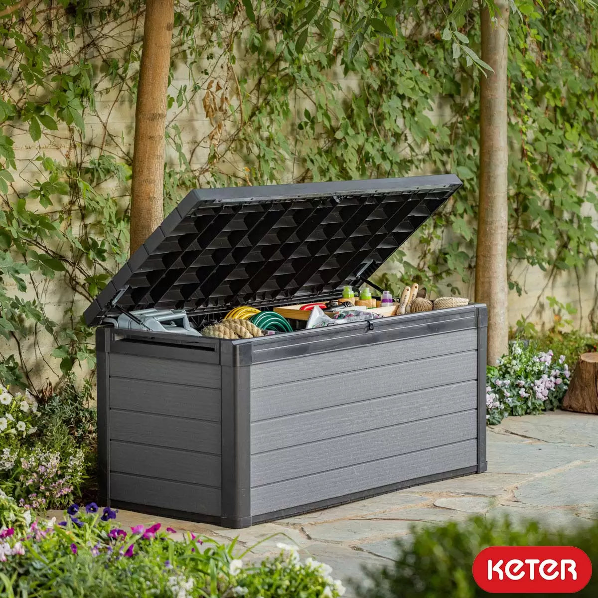 Keter Cortina 570L outdoor deck box in grey, featuring a wood-effect texture, closed securely on a clean patio setting.