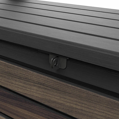 Front angle view of the brown Keter Rosewood 575L deck box featuring a realistic wood-grain texture, positioned on a modern stone patio next to outdoor green foliage.