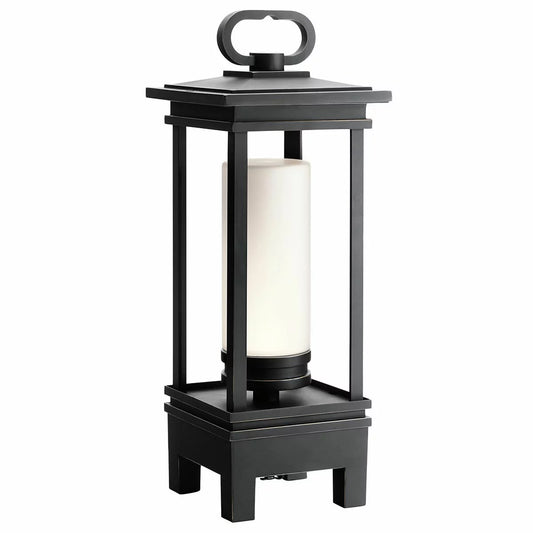 A Kichler South Hope rubbed bronze lantern with satined glass sitting on a wooden patio table, emitting a warm light.
