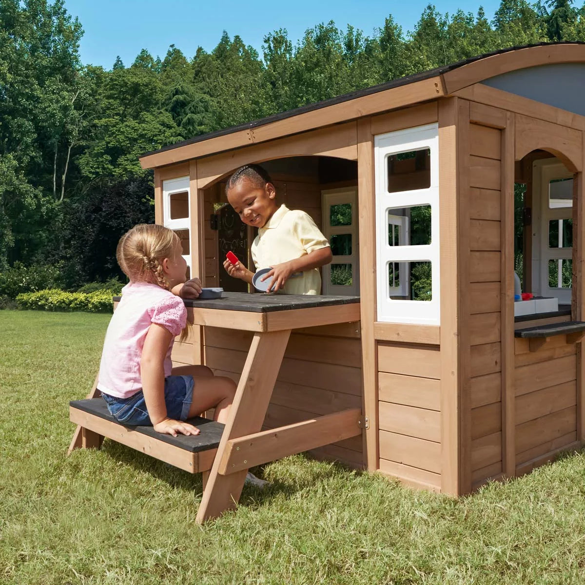 KidKraft Sunny Bluff brown wooden outdoor playhouse with curved double doors, picnic table, kitchen area, chalkboard shutters, and garden play space for children-2