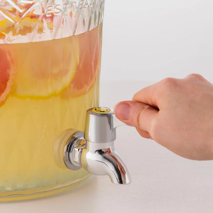 An 8-litre Kilner Diamond Drinks Dispenser filled with refreshing fruit-infused water, sitting on a wooden table, showcasing its faceted glass design and stainless steel clip-top.