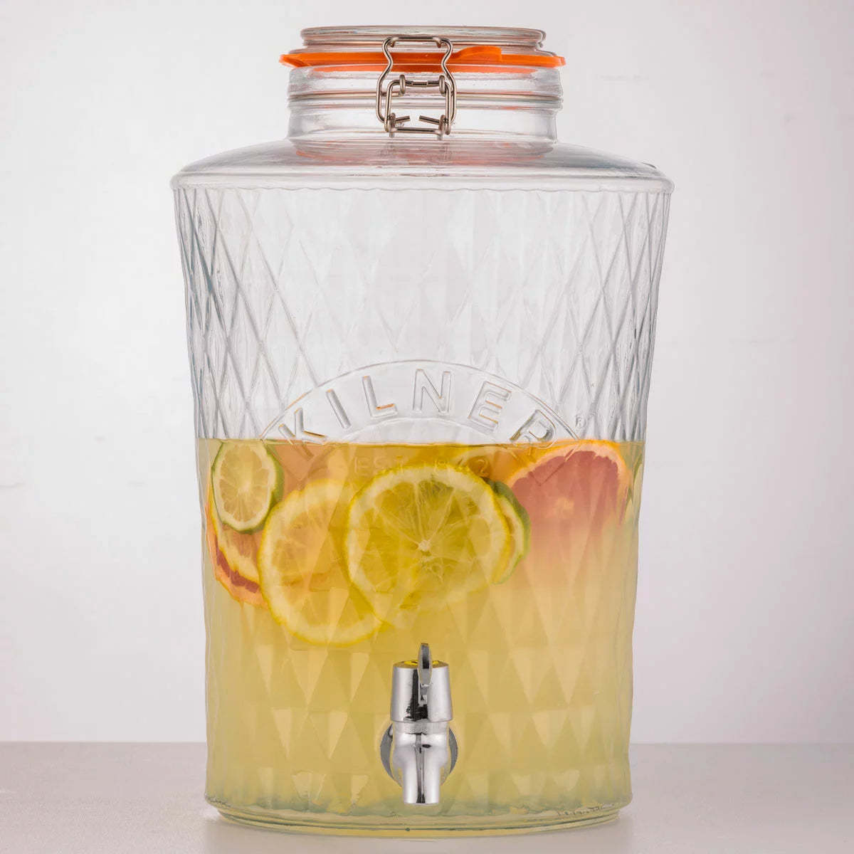 An 8-litre Kilner Diamond Drinks Dispenser filled with refreshing fruit-infused water, sitting on a wooden table, showcasing its faceted glass design and stainless steel clip-top.