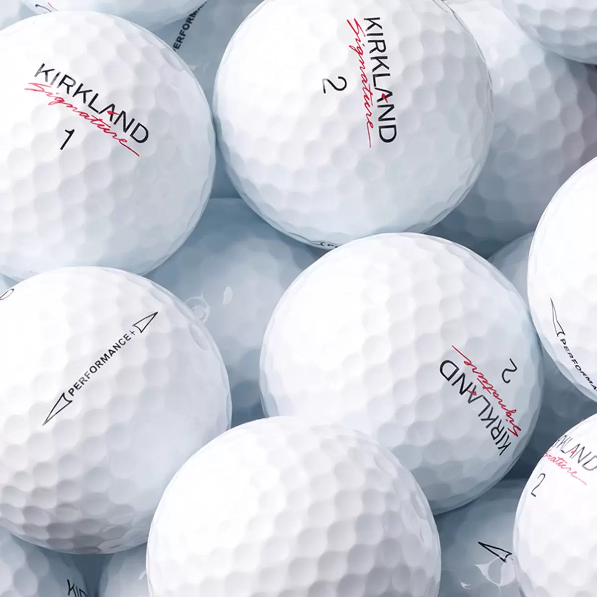High-angle studio shot of two dozen white Kirkland Signature 3-piece urethane golf balls arranged neatly inside their distinct red and black packaging on a dark reflective surface.