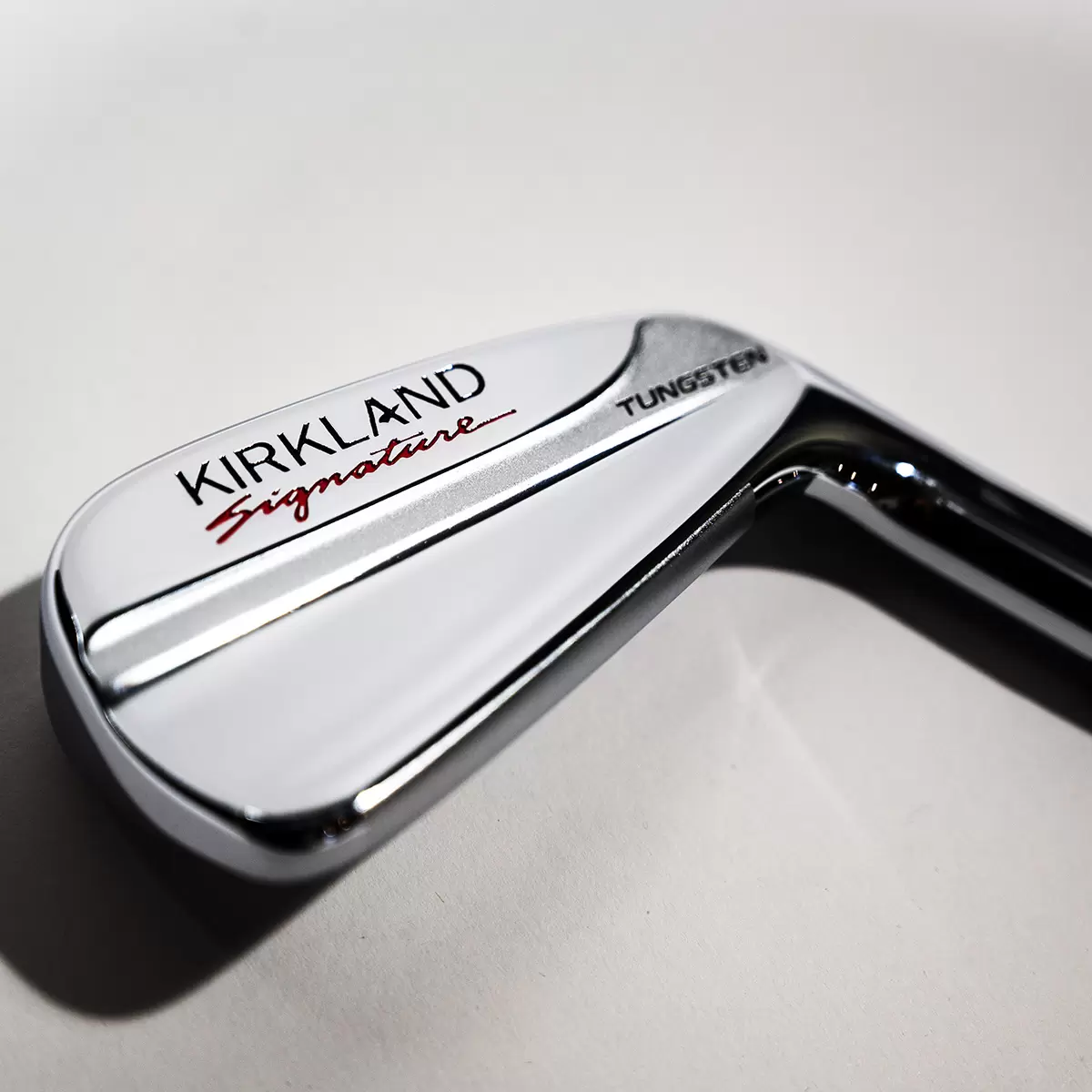 Side angle view of the chrome-finished Kirkland Signature stiff flex irons arranged neatly inside a premium leather golf bag on a manicured grass practice tee.