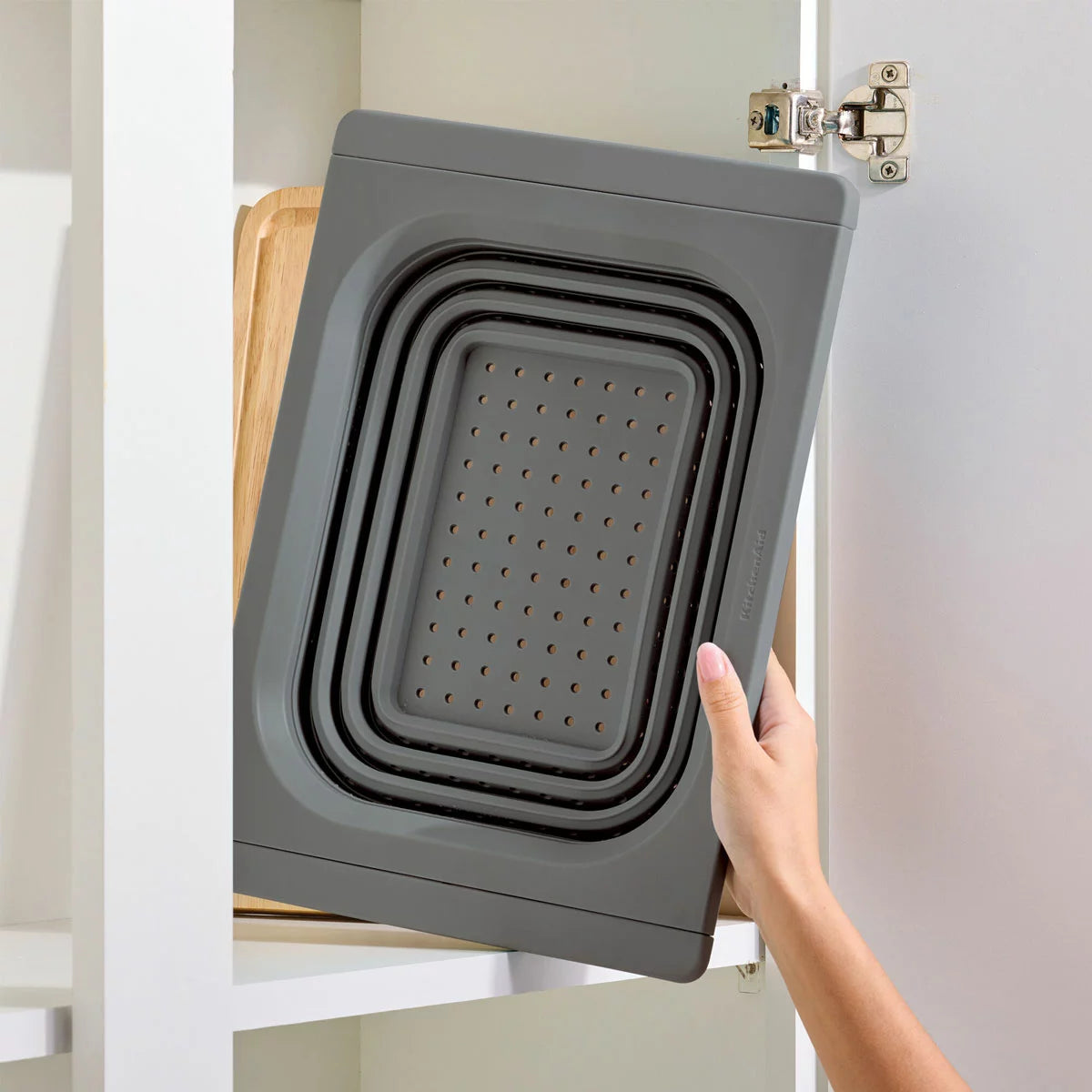 KitchenAid collapsible colander in grey and red showing space-saving flat design for kitchen storage.