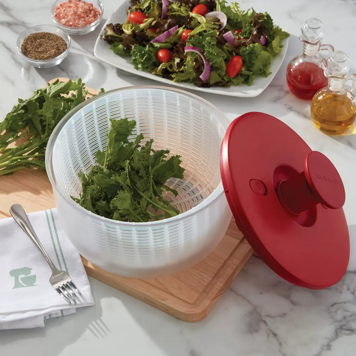 KitchenAid Salad Spinner in red and black available, demonstrating the pump-action drying mechanism on a clean kitchen countertop.