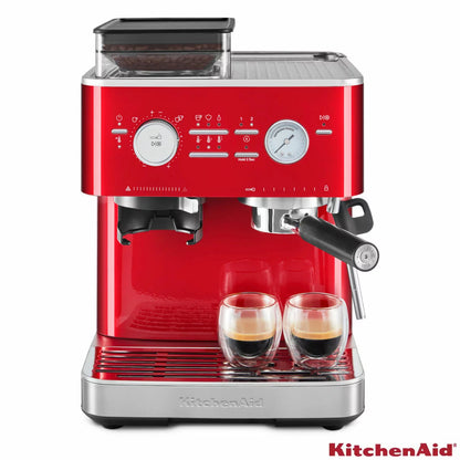 KitchenAid Candy Apple red semi automatic espresso machine with built in burr grinder, 58mm portafilter, and stainless steel milk pitcher on a clean kitchen countertop.