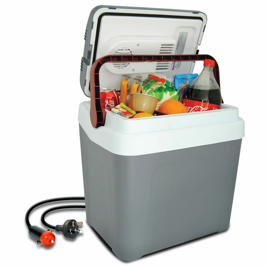 A grey Koolatron 12V Electric Cooler 24L with its sturdy locking handle upright, positioned in the open boot of a car during an outdoor weekend road trip.