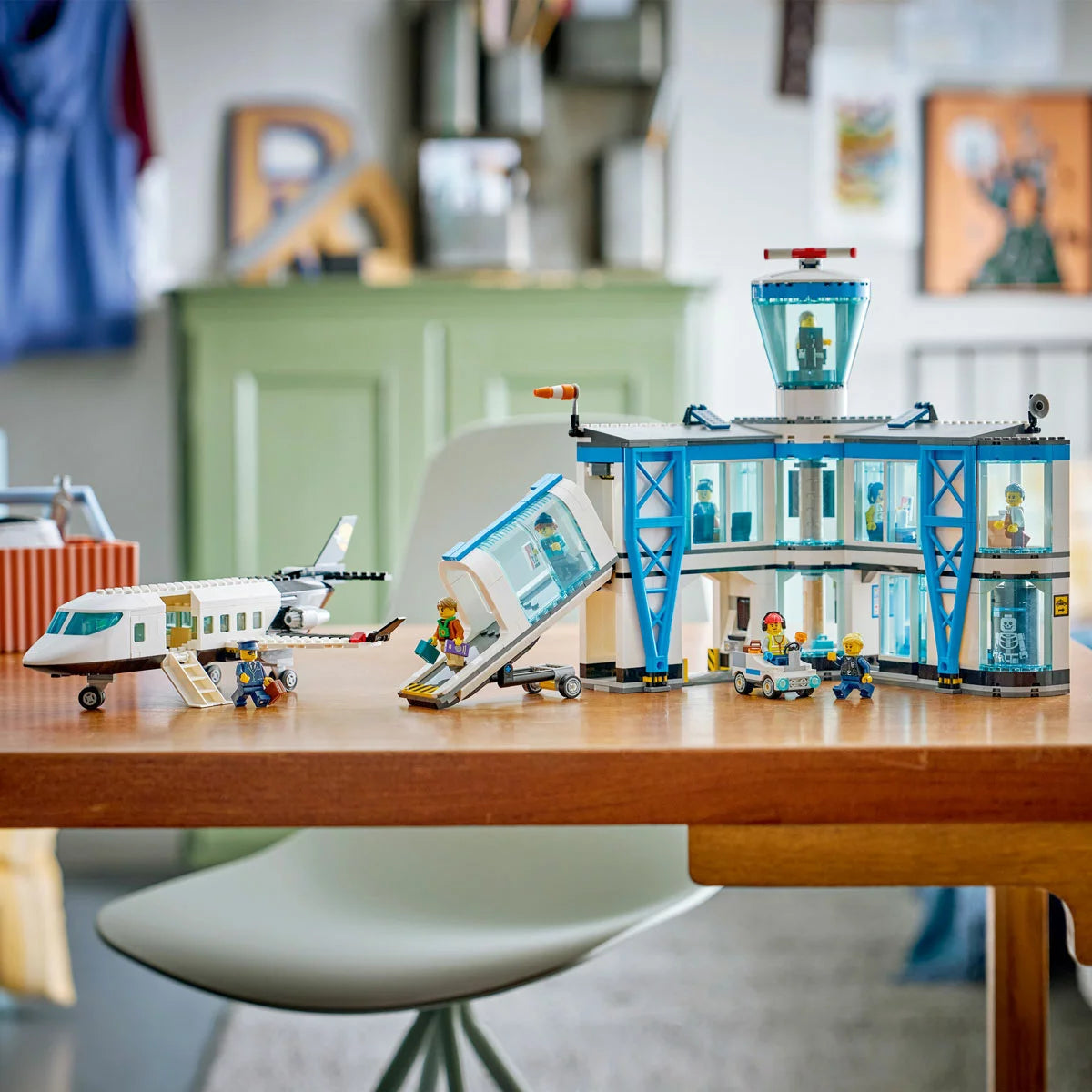 Wide shot of the LEGO City Airport 60502 set featuring a blue and white passenger plane attached to a yellow jet bridge, a multi-room terminal building, luggage tug, and nine minifigures on a bright surface.