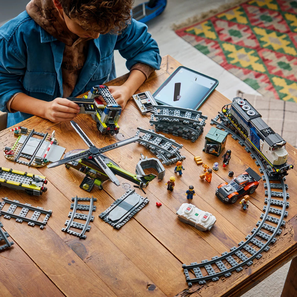 Three-quarter side view of the built blue LEGO 60508 police train traveling on tracks while a red helicopter flies overhead with a grabbing claw.