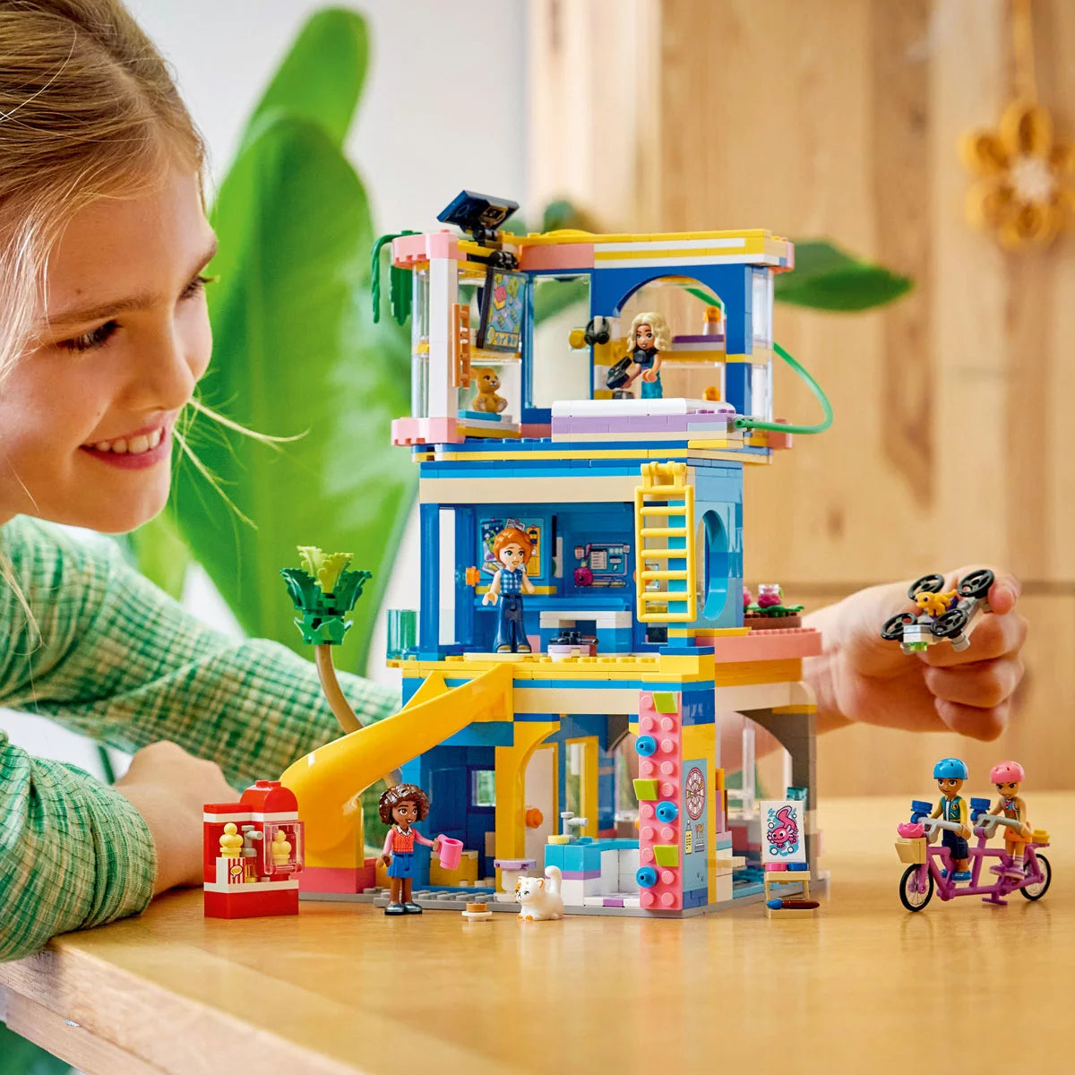 Front angle view of the colorful multi-story LEGO Friends Heartlake City Club House 42689 set featuring a red slide, zipline, climbing wall, five mini-dolls, and three pet figures on a clean white surface.