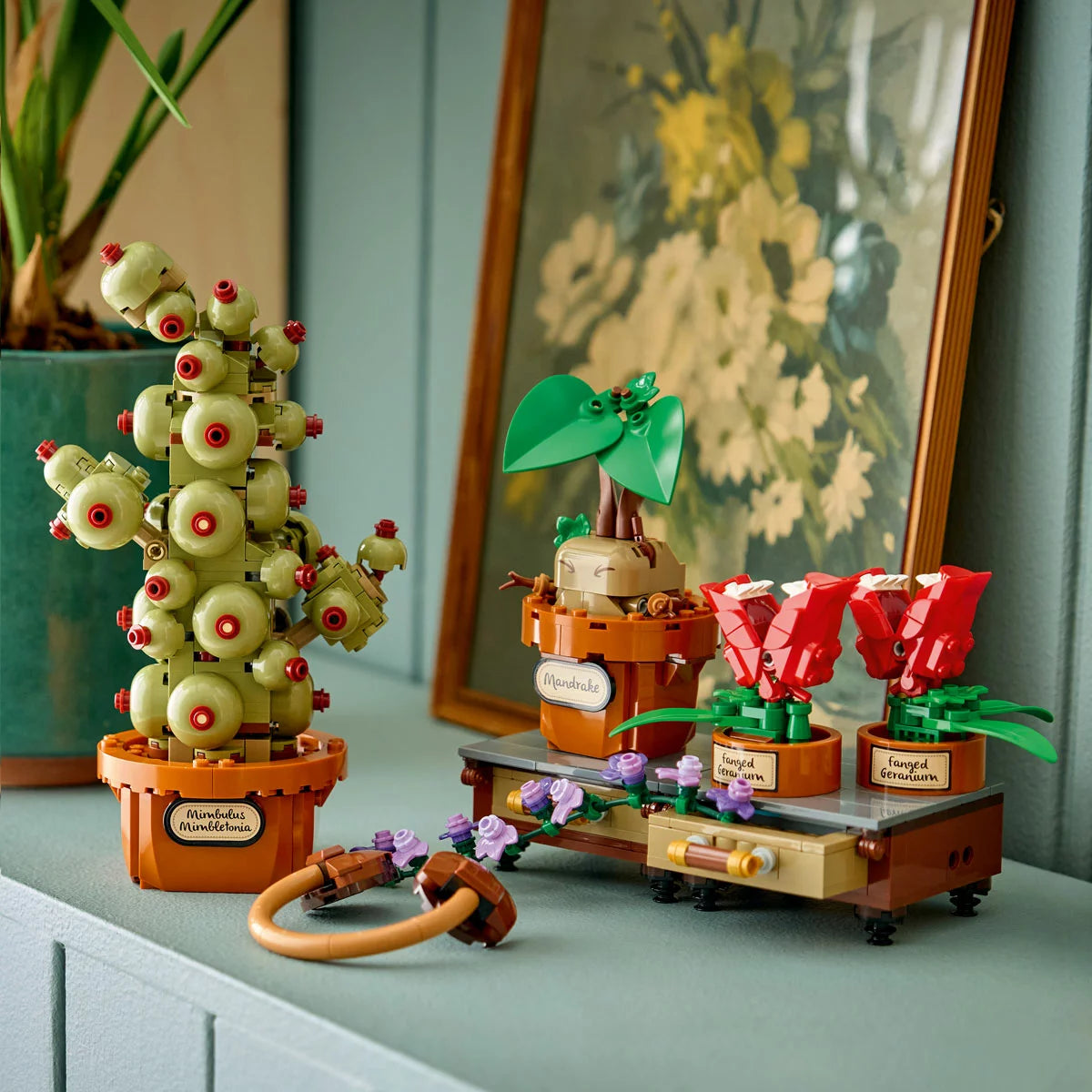 ye-level view of three brick-built LEGO Harry Potter Herbology Plants 76474—a Mandrake, Fanged Geranium, and Mimbulus Mimbletonia—arranged on a brown display table with green vines and yellow earmuffs against a neutral backdrop.