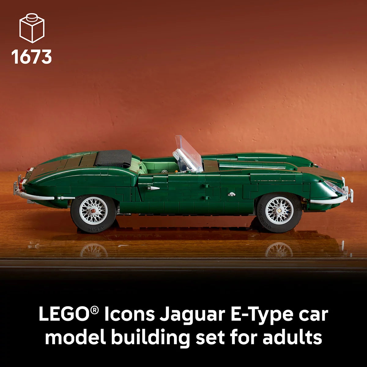 Three-quarter angle of built British green LEGO Icons Jaguar E-Type model car with wire-style wheels and dark interior on a dark wooden display surface.
