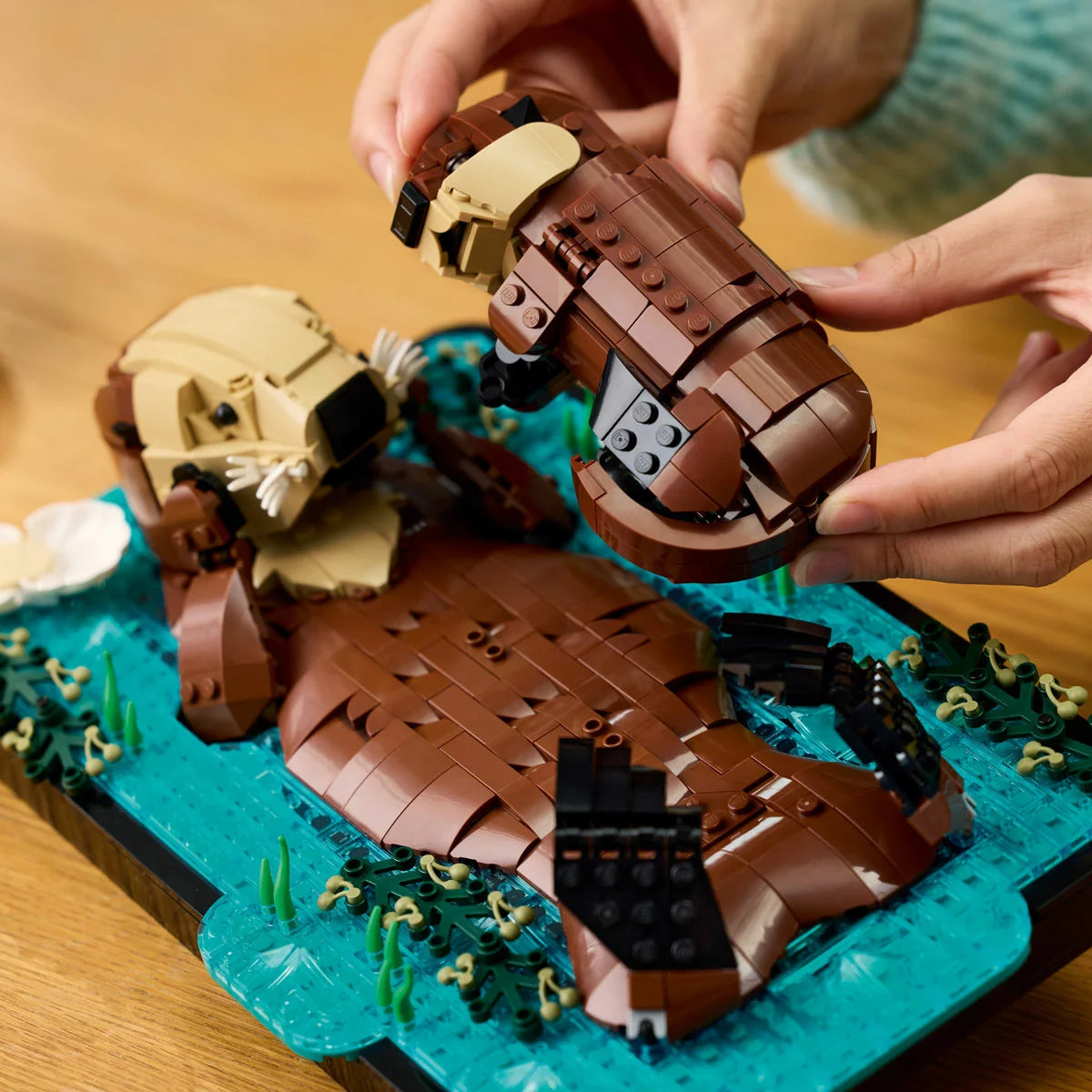 Side view of the built LEGO Ideas 21366 floating sea otters model featuring a brown mother otter holding a pup on its belly across a blue brick water base.