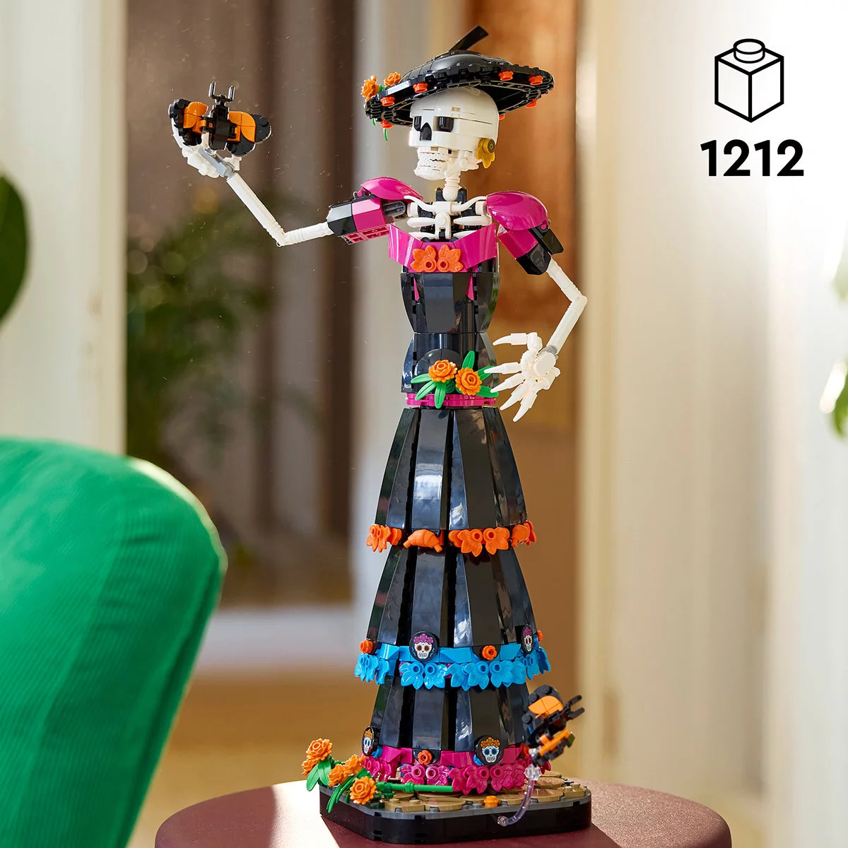 LEGO Ideas La Catrina model figure standing on a marigold-covered base wearing a wide-brimmed hat with colorful skull prints and orange flowers.
