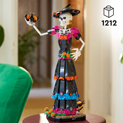 LEGO Ideas La Catrina model figure standing on a marigold-covered base wearing a wide-brimmed hat with colorful skull prints and orange flowers.