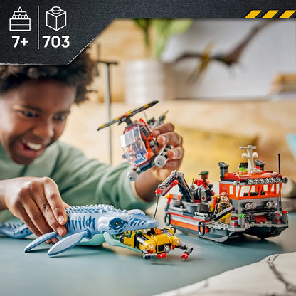LEGO Jurassic World Mosasaurus model set 77983 featuring a large blue-grey dinosaur attacking a cargo boat with helicopter and three minifigures on a plain background.