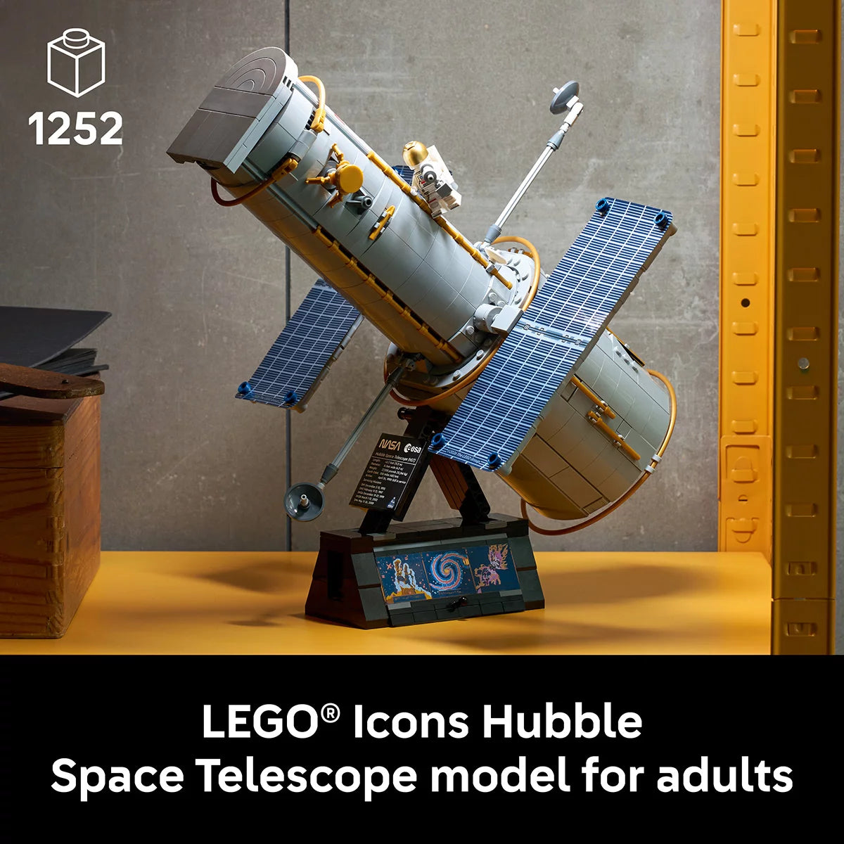 LEGO Icons NASA Hubble Space Telescope model mounted on its display stand alongside an astronaut minifigure and informative plaque.