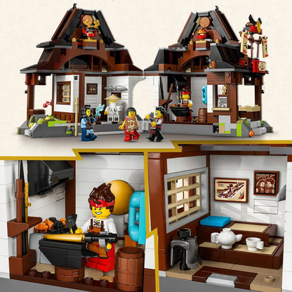 Three-quarter front view of the opened LEGO Ninjago Four Weapons Blacksmith 71858 set showing the detailed interior forge, weapons rack, upper bedroom, and six minifigures arranged on a grey surface.
