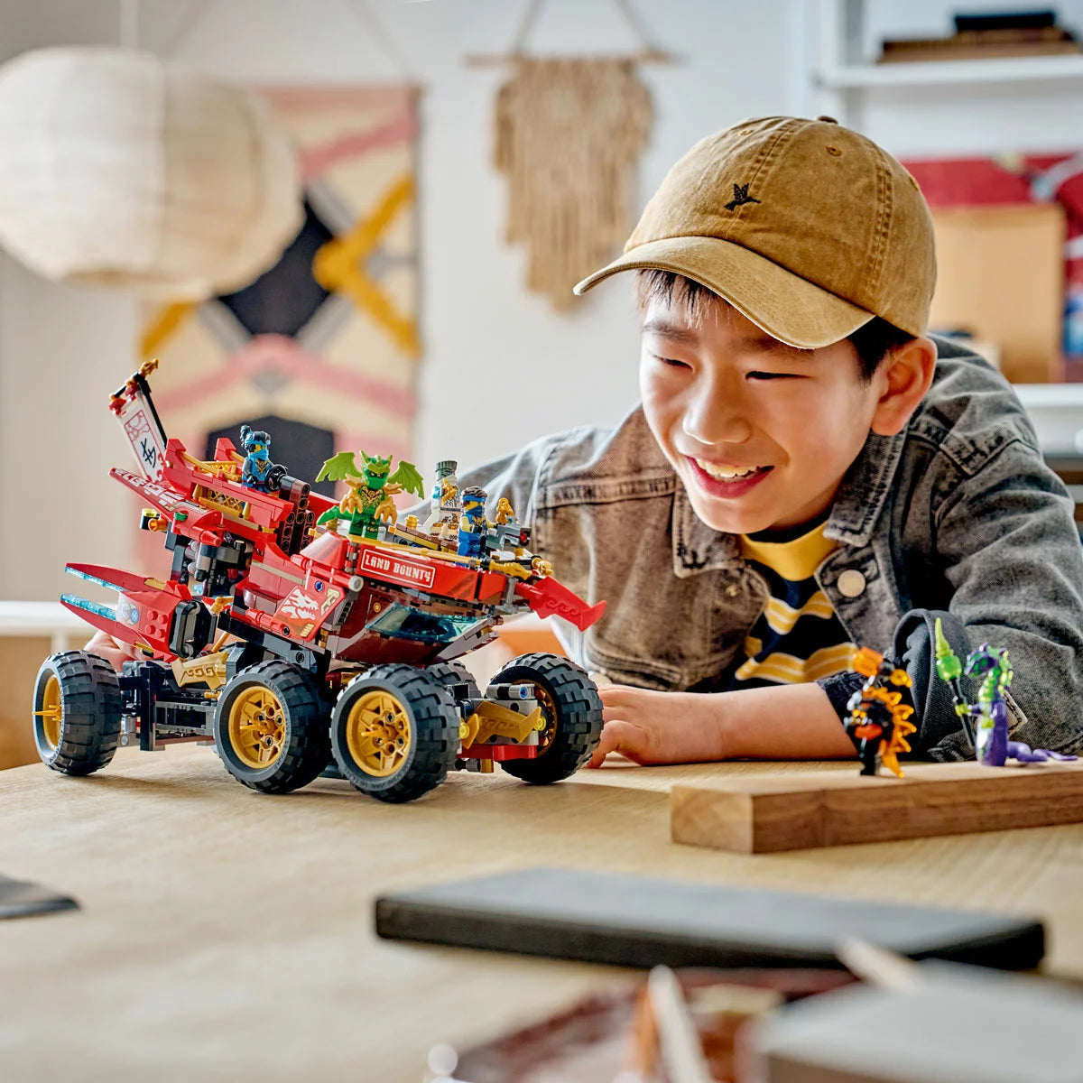 Three-quarter studio view of the built LEGO Ninjago 71869 Land Bounty truck showing its six large gold wheels, blue flags, and detachable flying ship module splitting from the chassis.