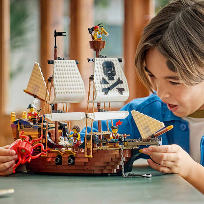 Front angle view of built LEGO Creator 31387 pirate ship model with sails raised, cannons ready, sea monster, and pirate minifigures on a plain surface.