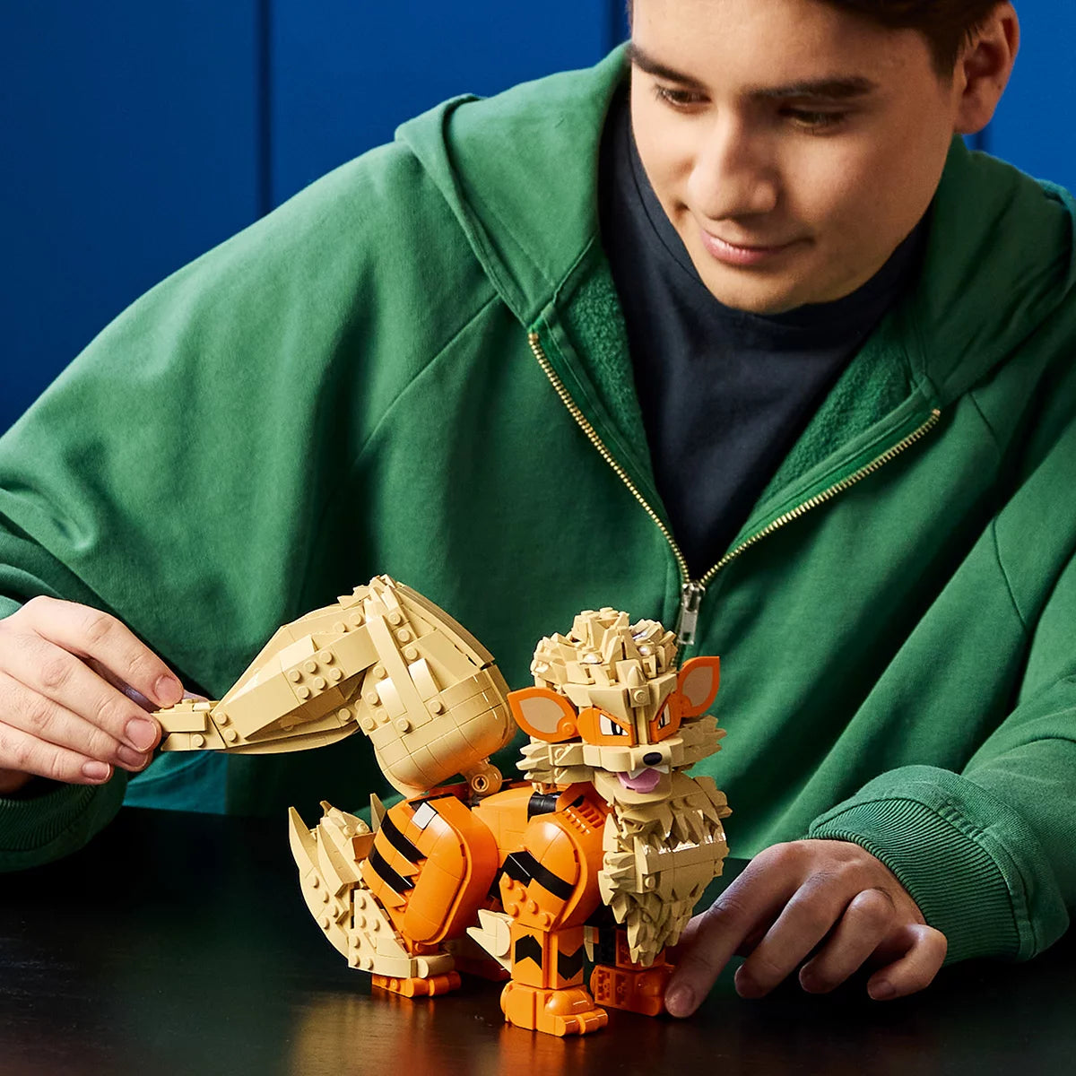 Front three-quarter view of the assembled orange and cream LEGO Pokémon Arcanine figure posed dynamically on a clean dark wood desk.