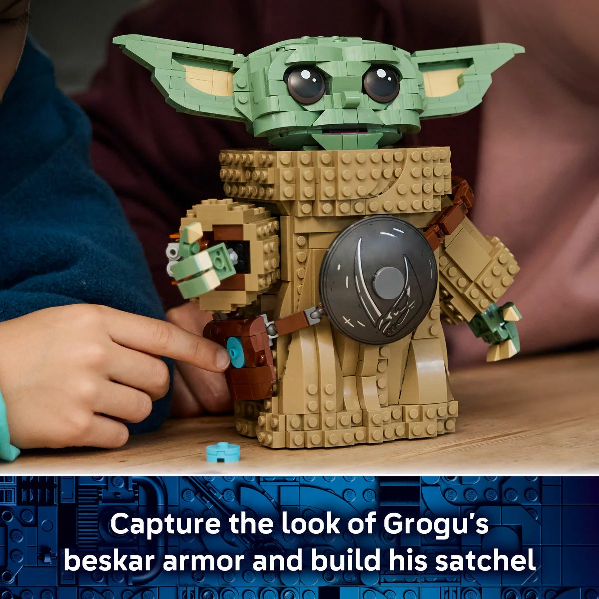 Front view of the built LEGO Star Wars 75446 Grogu figure wearing silver beskar armor and holding a blue cookie accessory next to his information display plaque.