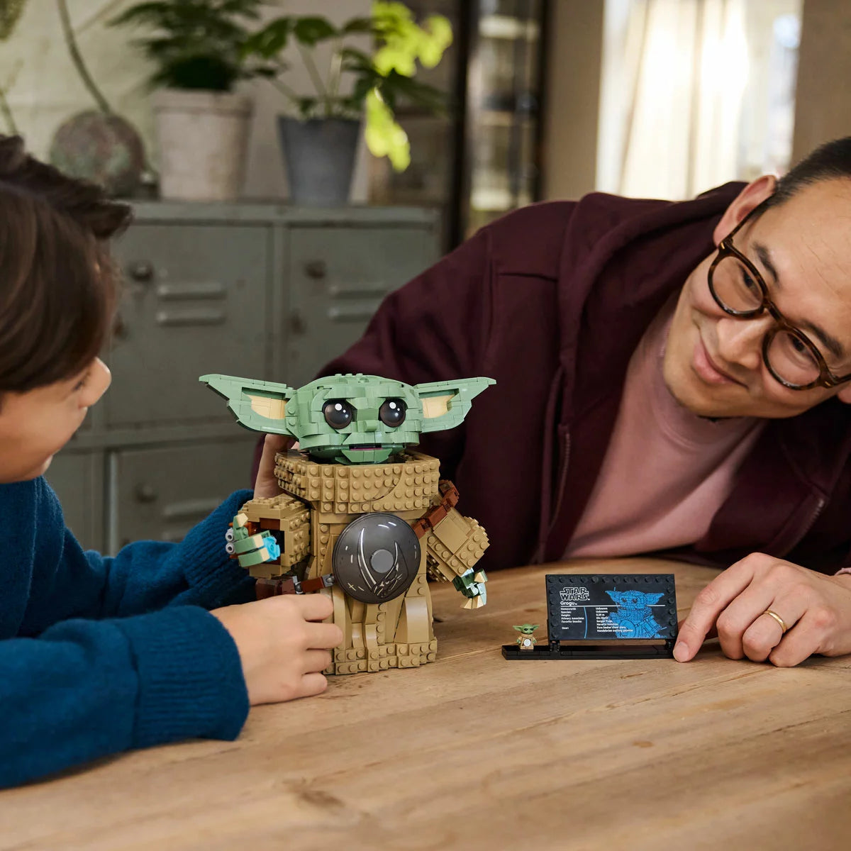 Front view of the built LEGO Star Wars 75446 Grogu figure wearing silver beskar armor and holding a blue cookie accessory next to his information display plaque.