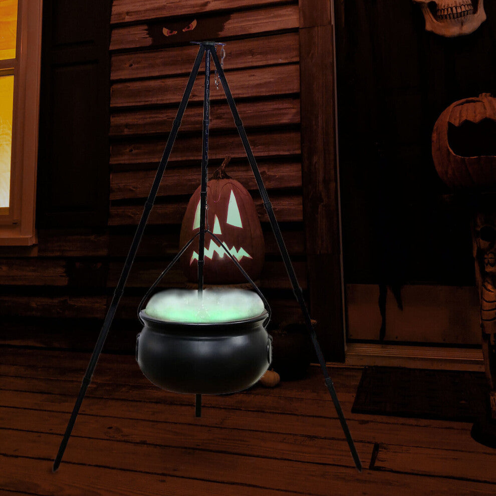 A large black witches cauldron hanging on a tripod stand in an outdoor yard setting, styled with atmospheric Halloween lighting and fog.