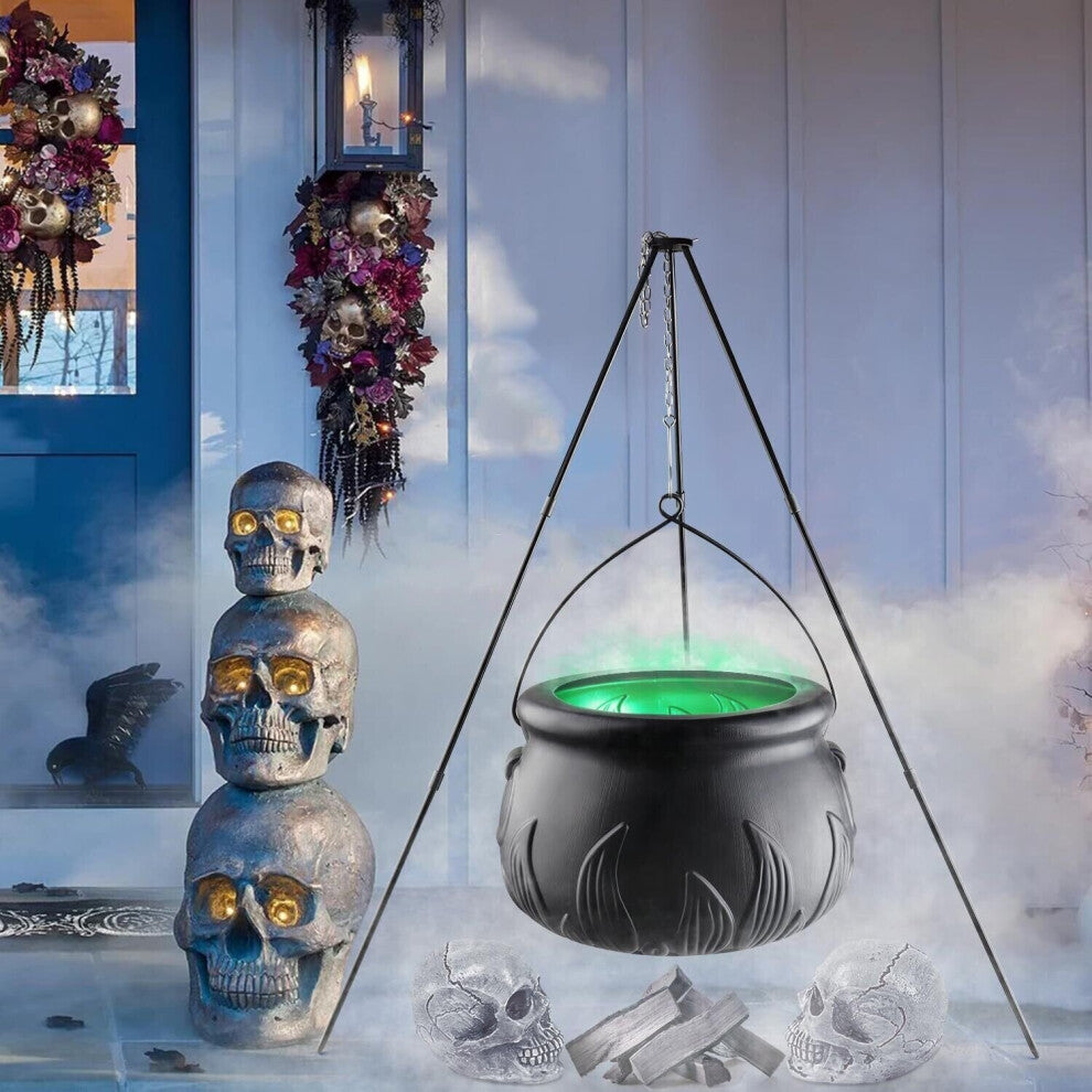 A large black witches cauldron hanging on a tripod stand in an outdoor yard setting, styled with atmospheric Halloween lighting and fog.