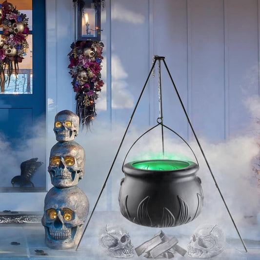 A large black witches cauldron hanging on a tripod stand in an outdoor yard setting, styled with atmospheric Halloween lighting and fog.