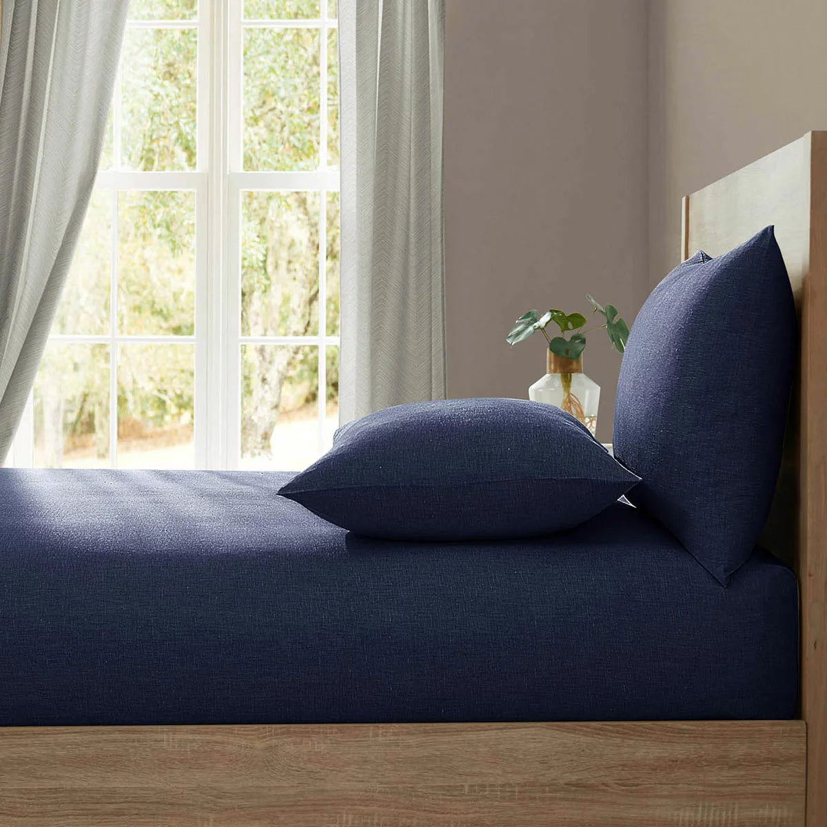Deep navy blue Lazy Linen fitted sheet wrapped snugly around the corner of a thick mattress demonstrating its soft washed texture.