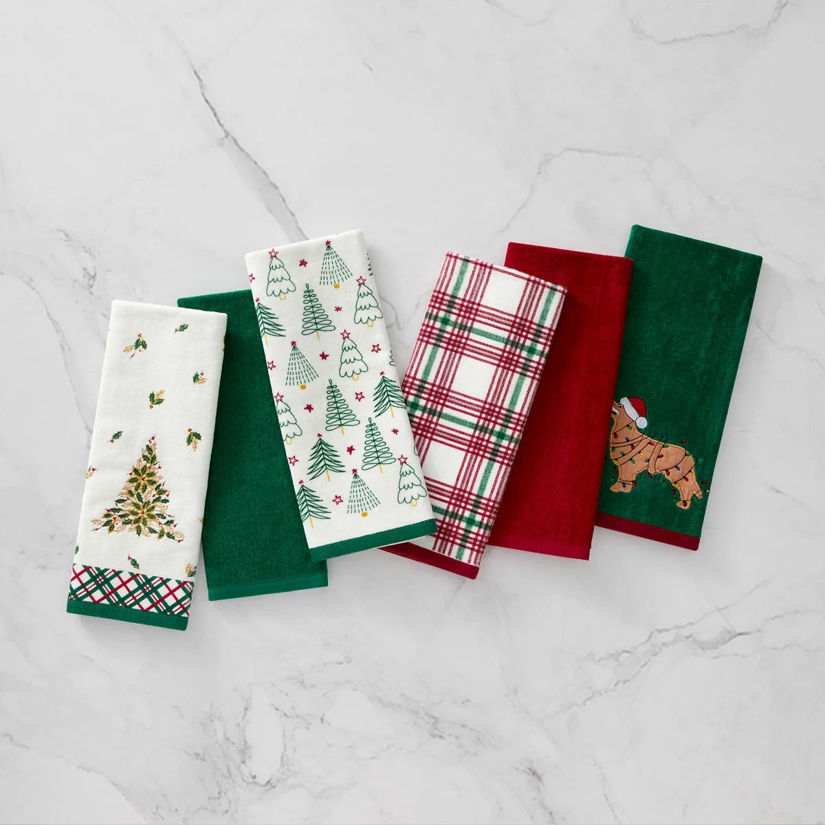 Lenox Holiday Kitchen Towels 6 Pack featuring three distinct red and green seasonal cotton patterns folded neat on a wooden countertop.