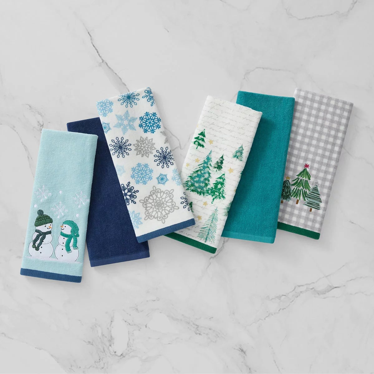 Lenox Holiday Kitchen Towels 6 Pack featuring three distinct red and green seasonal cotton patterns folded neat on a wooden countertop.