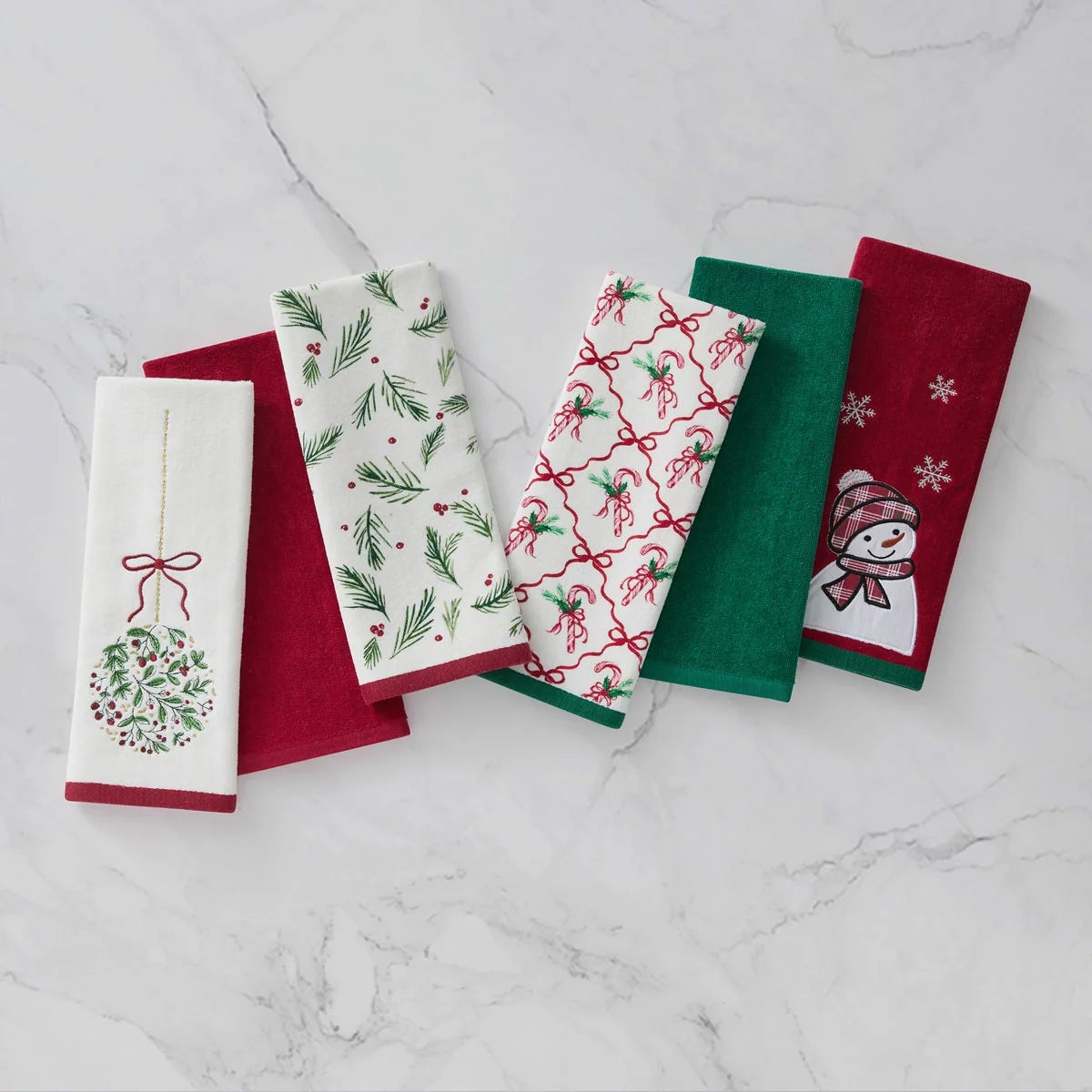 Lenox Holiday Kitchen Towels 6 Pack featuring three distinct red and green seasonal cotton patterns folded neat on a wooden countertop.