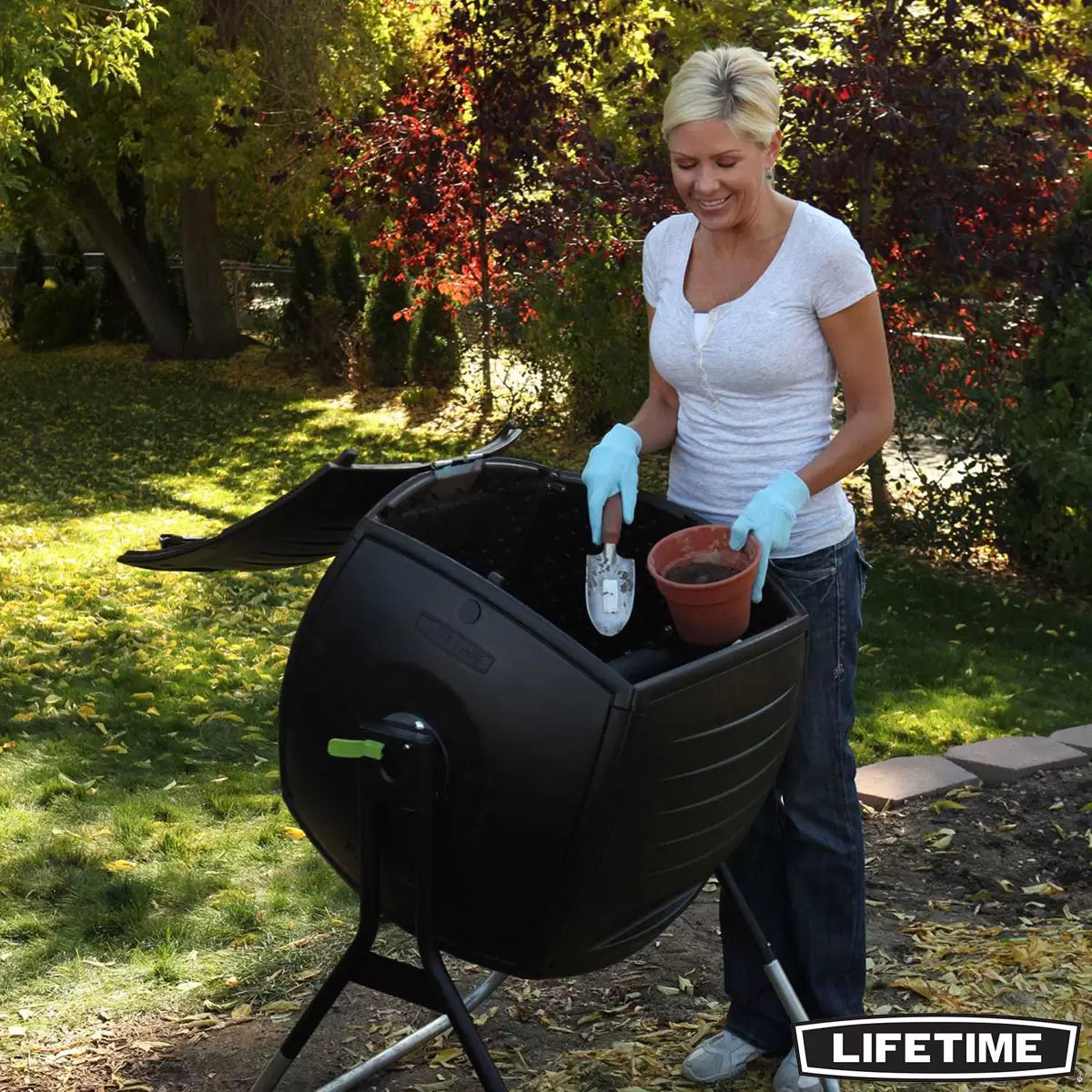 A black Lifetime 189 Litre tumbling composter on a sturdy galvanized steel base in a garden setting.