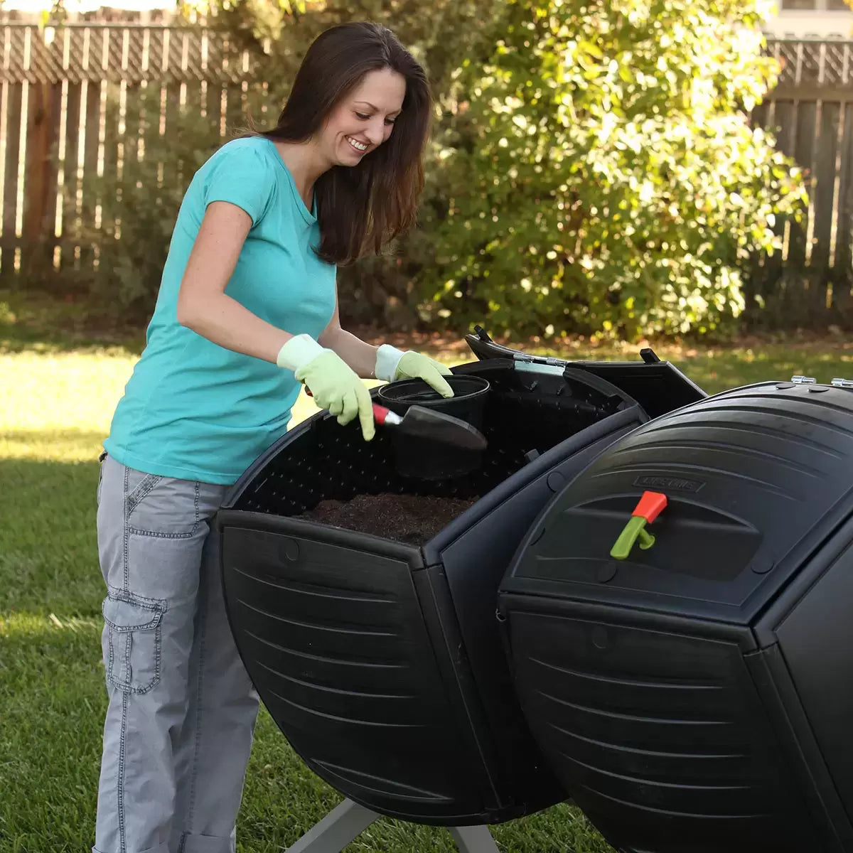 A side-by-side view of the Lifetime 378L dual tumbling composter on a sturdy steel base, situated on a clean garden patio, showing the black panels and red processing indicators.
